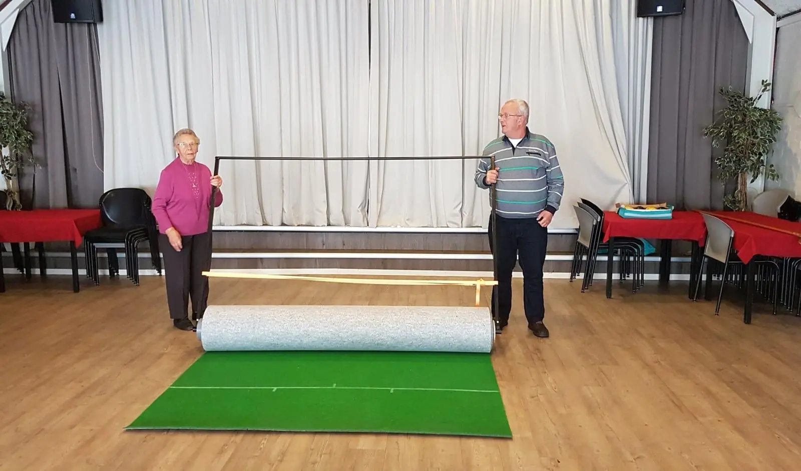 Two people unrolling a koersbal mat from its storage tube